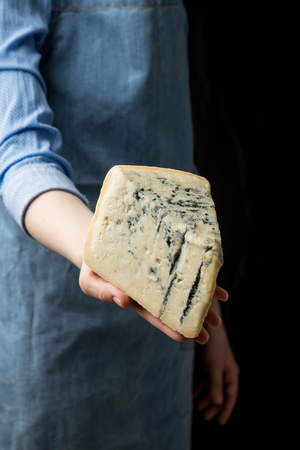 Woman in apron holding piece of blue cheese Gorgonzola on dark background. Studio shotの写真素材