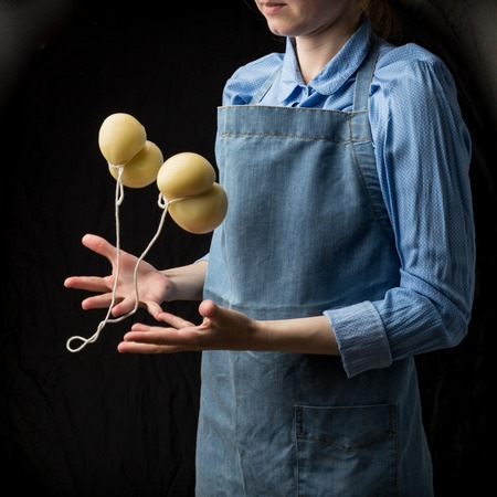 Gourmet italian cheese scamorza in hands of cheese maker in blue apron on black background. Studio shotの写真素材