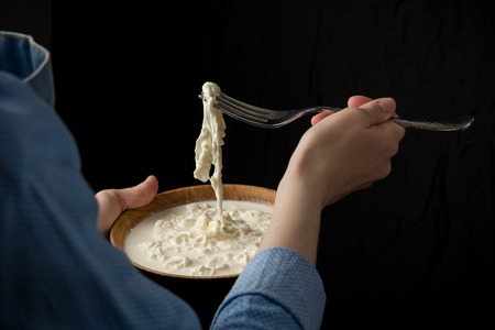 Woman in blue apron holding bowl with stracciatella mozzarella cheese on dark background. Studio...