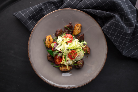 Chicken liver salad with cherry tomatoes and salad mix on black backgroundの写真素材