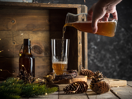 pouring beer into a tall glass on wooden background with christmas lights. Studio shotの写真素材