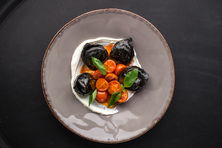 Traditional Italian black ravioli with cherry tomatoes on black background top viewの写真素材