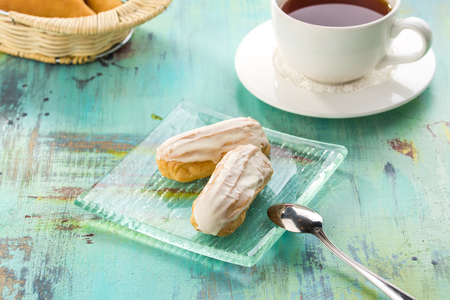 Homemade eclair dessert with vanilla and cup of tea on blue wooden table side view
