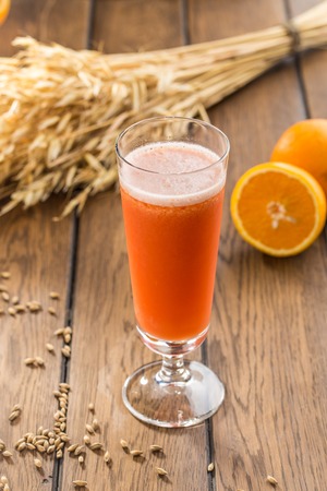 Carrot juice in glass and fresh orange and wheat spikes on wooden table side viewの写真素材