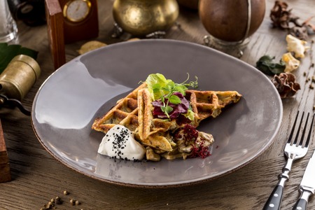 Savory waffles with mushroom and creamy sauce on plate on a wooden table side viewの写真素材