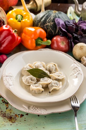 Russian meat dumplings pelmeni with bay leaf and fresh vegetables on blue wooden table side viewの写真素材