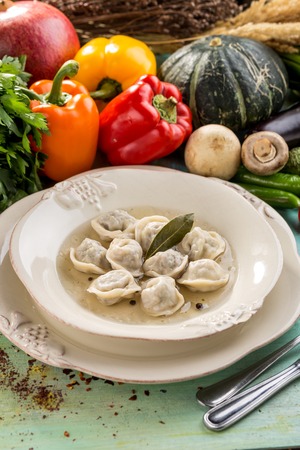 Russian meat dumplings pelmeni with bay leaf and fresh vegetables on blue wooden table side viewの写真素材