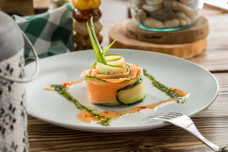 Restaurant Starter with Raw Salted Salmon Slices and Cucumber on white plate on wooden table side viewの写真素材