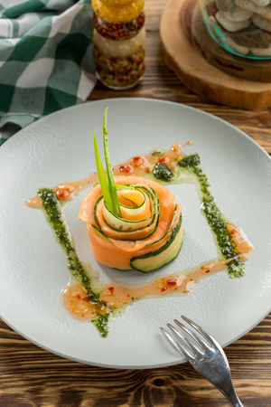 Restaurant Starter with Raw Salted Salmon Slices and Cucumber on white plate on wooden table side viewの写真素材