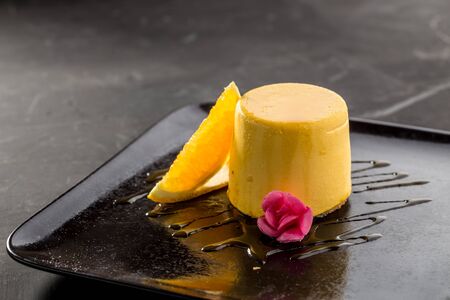 Mango pudding jelly dessert on black plate on black background side view