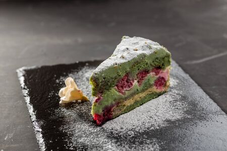 Homemade Pistachio Raspberry Cake with Cream Cheese on stone plate on black background side viewの写真素材