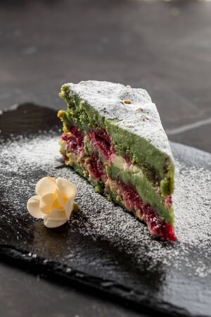 Homemade Pistachio Raspberry Cake with Cream Cheese on stone plate on black background side viewの写真素材