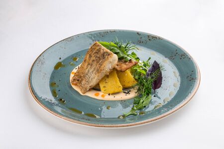 Fried white fish fillet with potatoes and greens on blue plate isolated on white background side...