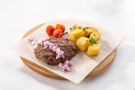 Grilled Beef Steak with Potato, red onion and tomato on wooden board isolated on white background...