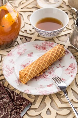 sweet wafer tube from thin dough and glass of black tea on oriental wooden table side view