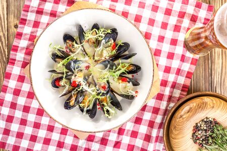 Cooked fresh mussels on white plate with glass of beer on wooden table top viewの写真素材