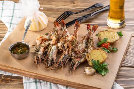 Grilled prawns shrimps Langostino Austral on wooden board and glass of beer on wooden table side viewの写真素材