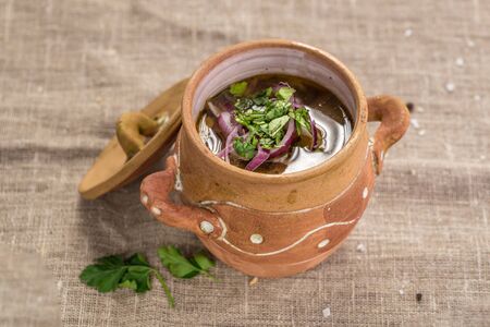 Homemade lamb soup with vegetables in clay pot on tablecloth top viewの写真素材