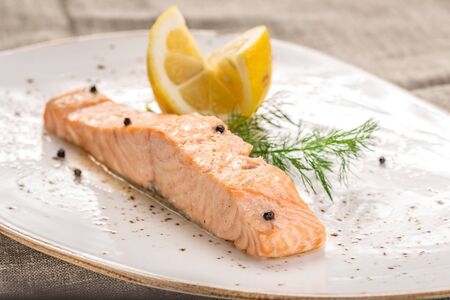 Steamed salmon with lemon on white plate on grey tablecloth side viewの写真素材