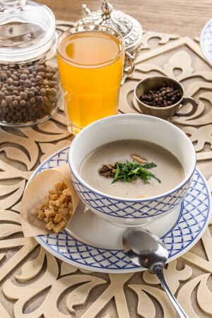 Bowl of mushroom cream soup with croutons and glass of yellow drink on oriental wooden table side viewの写真素材