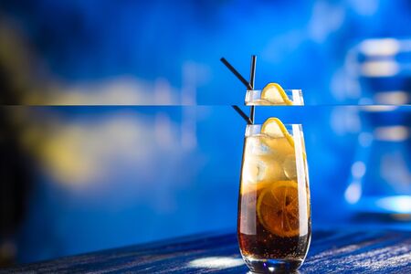 Rum cola cocktail with ice cubes and lemon on club table background side view