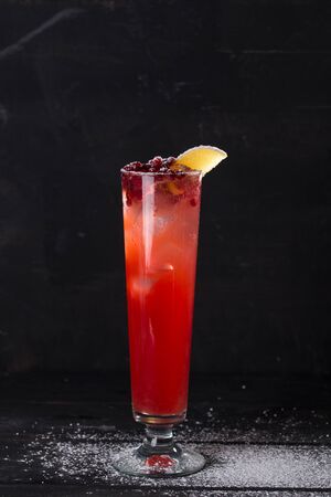 Cranberry cocktail with lemon and ice decorated with powdered sugar on black background side viewの写真素材