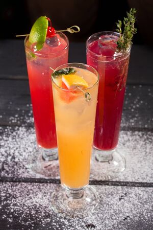 three glasses of fruit red yellow lemonade with ice in highball glasses on black background side viewの写真素材