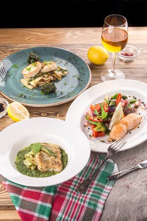 cooked salmon, trout and fish patties with different garnish and glass of white wine on wooden table side viewの写真素材