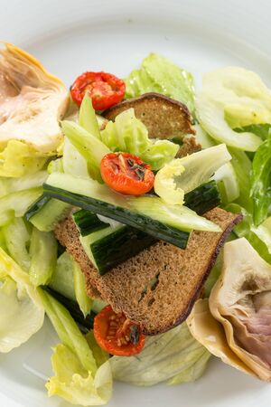 Salad with artichokes, cherry tomatoes, lettuce and rye bread on white plate close up side viewの写真素材