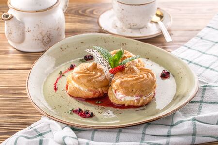 Cream puff cakes profiterole filled with whipped cream served with strawberry jam on wooden table...