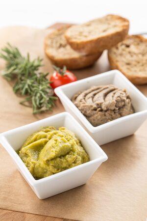 homemade guacamole and mushroom paste in bowl and sliced bread on wooden board isolated on white background side viewの写真素材