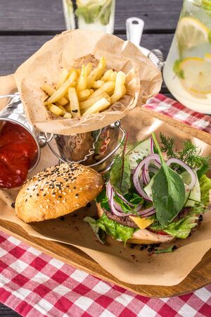 burger with cheese, red onion, French fries and lemonade on black wooden table side viewの写真素材