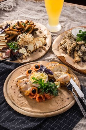 Assorted beer snacks smoked fish, cheese, roastbeef, bread croutons on wooden platter and glass of beer side viewの写真素材