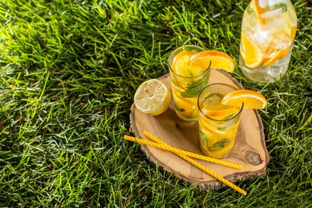 cold lemonade drink with orange and mint in tall glass on green grass lawn wooden background top viewの写真素材