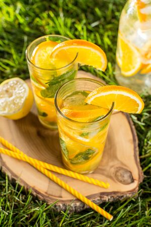 cold lemonade drink with orange and mint in tall glass on green grass lawn wooden background top viewの写真素材