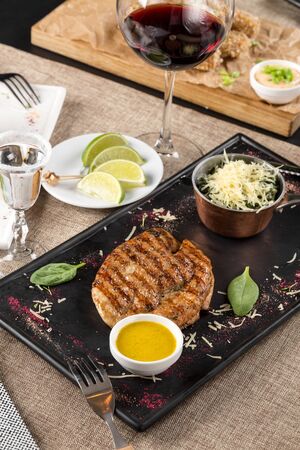 Grilled chicken fillet on slate plate with glass of red wine on the table at restaurant side viewの写真素材