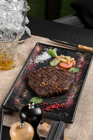 Grilled Ribeye Steak with vegetable salad on stone board on the table at restaurant side viewの写真素材