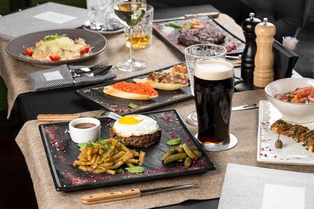 Fried minced beef steak with egg, fried potatoes and glass of dark beer on the table at restaurant side viewの写真素材