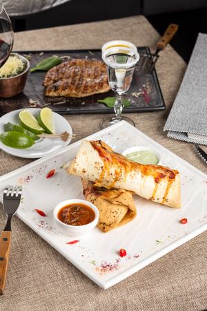 Mexican restaurant fast food wrapped burritos with meat, sauces and tequila shot on the table at restaurant side viewの写真素材