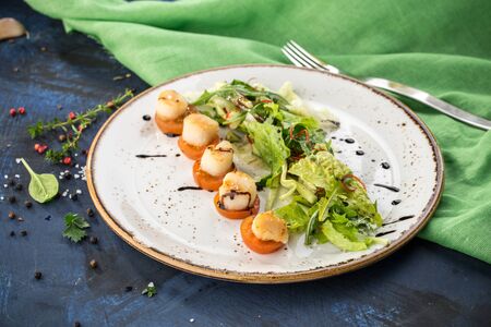 Fresh seared sea scallops with tomato and salad on white plate on blue and green background side viewの写真素材