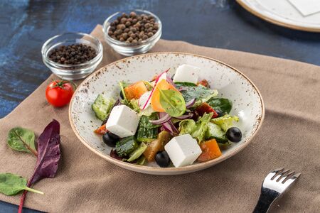 Fresh Greek salad in bowl with olives tomato feta cheese cucumber and onion on textile napkin side viewの写真素材