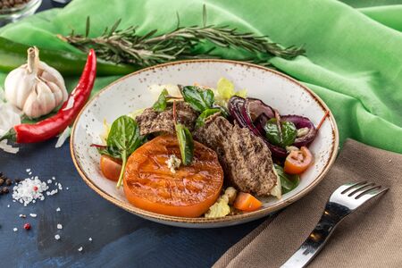 Warm salad with grilled veal, tomato, onion and lettuce on blue green background side viewの写真素材