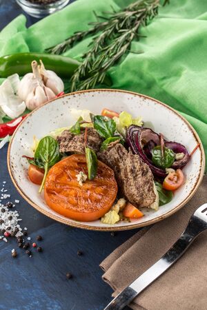Warm salad with grilled veal, tomato, onion and lettuce on blue green background side viewの写真素材