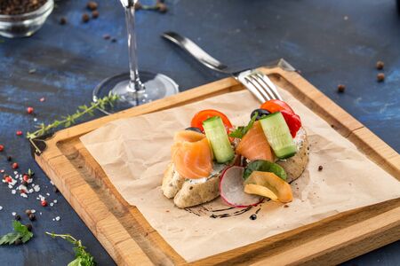 Small sandwich with salmon, tomato and cucumber on wooden board on blue background side viewの写真素材