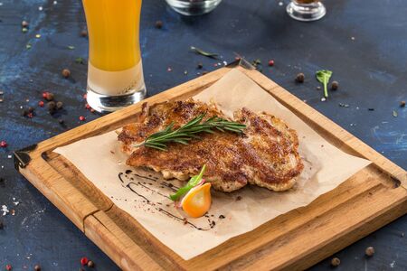 Chicken schnitzel grilled on wooden board with glass of beer on blue background side viewの写真素材