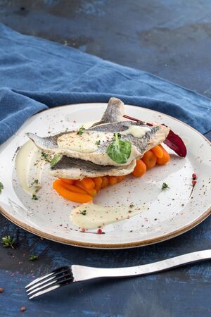 Tasty healthy fish fillet with baby carrots on white plate on blue background side viewの写真素材