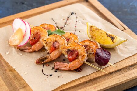 grilled prawns shrimps on skewer and lemon slice on wooden board on blue background side viewの写真素材