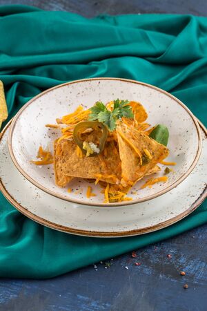 Nacho Chips with cheese and Jalapeno on white plate on turquoise background side viewの写真素材