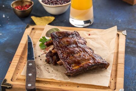 Grilled barbecue spareribs and bbq sauce on wooden board and glass of beer on blue background side viewの写真素材
