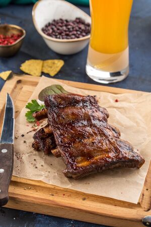 Grilled barbecue spareribs and bbq sauce on wooden board and glass of beer on blue background side viewの写真素材